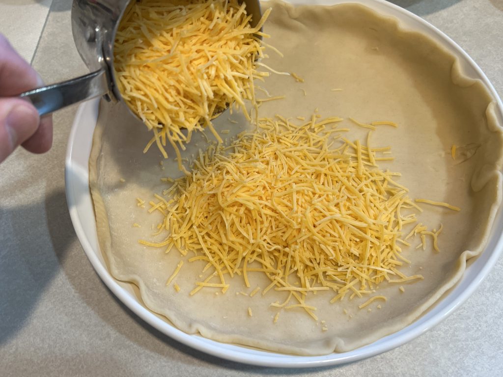 dumping cheese in pie plate for quiche recipe