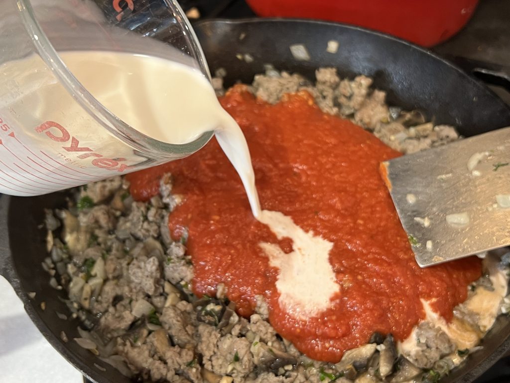 half and half being poured into skillet with pasta sauce for cavatappi pasta recipe.